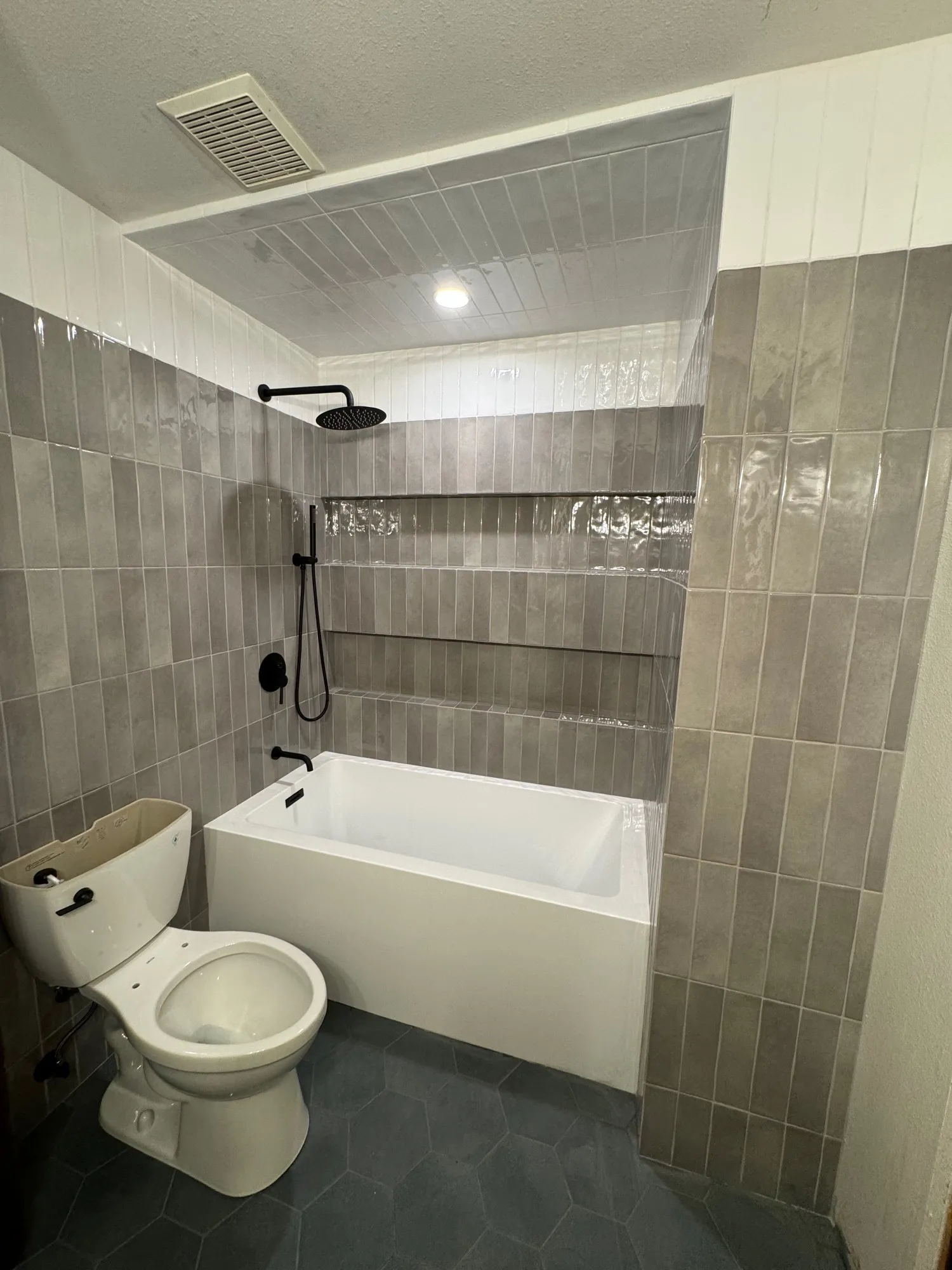 Tub-shower in gray vertical subway tile with a white accent stripe and hexagon floor