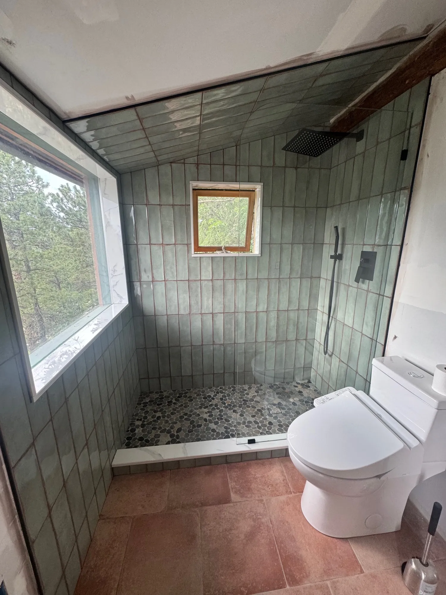 Sage-green vertical tile shower with a pebble pan and terracotta floor