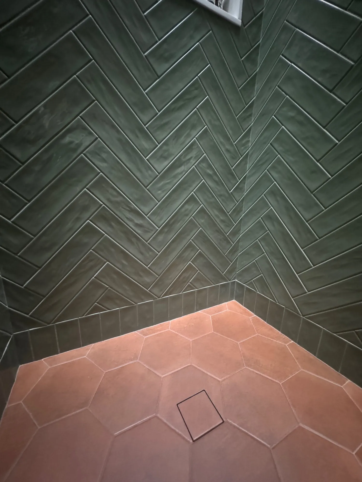 Detail of glossy green herringbone wall tile meeting a terracotta hexagon floor