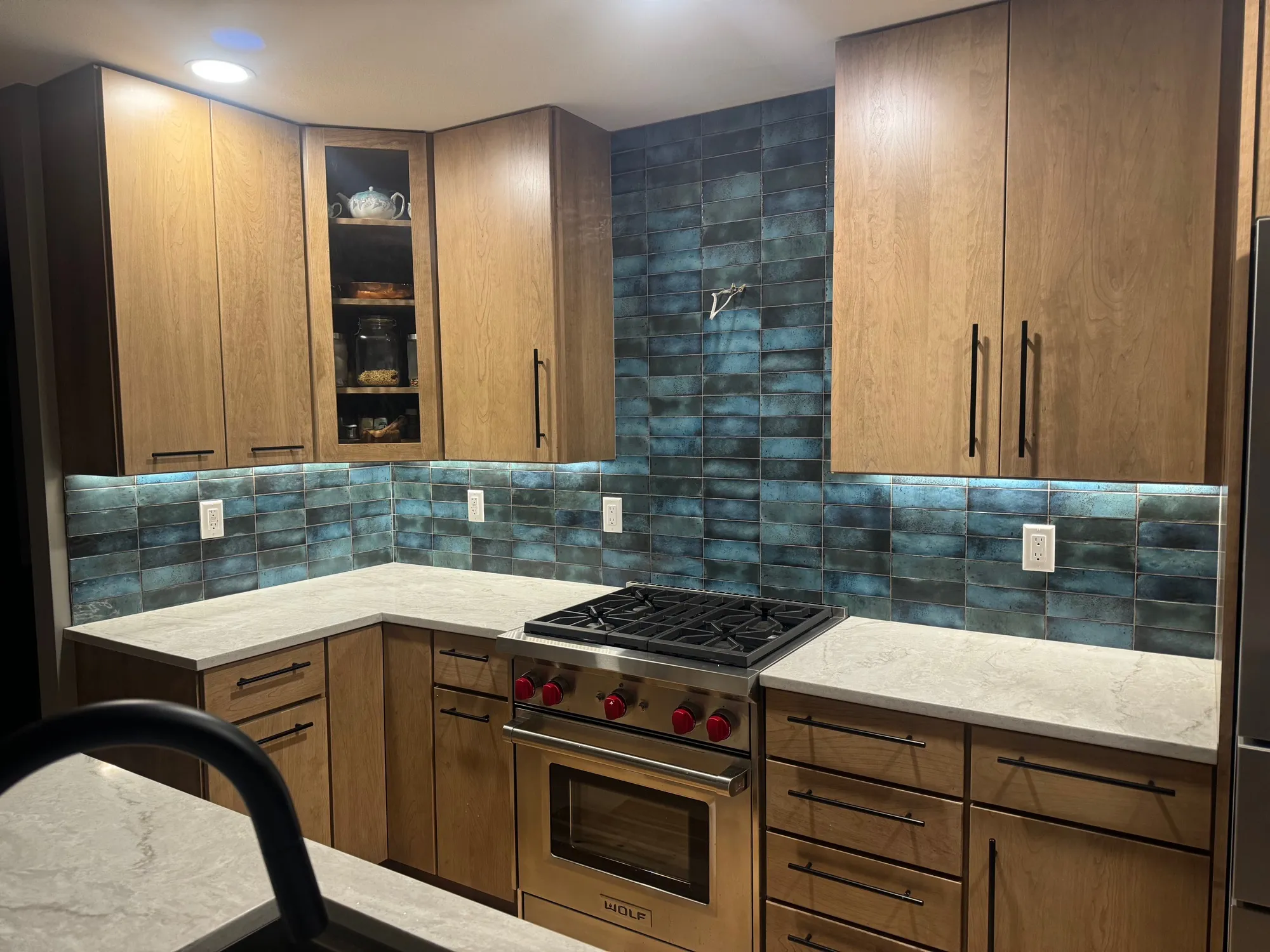 Iridescent teal glazed subway tile backsplash with wood cabinets and a pro range