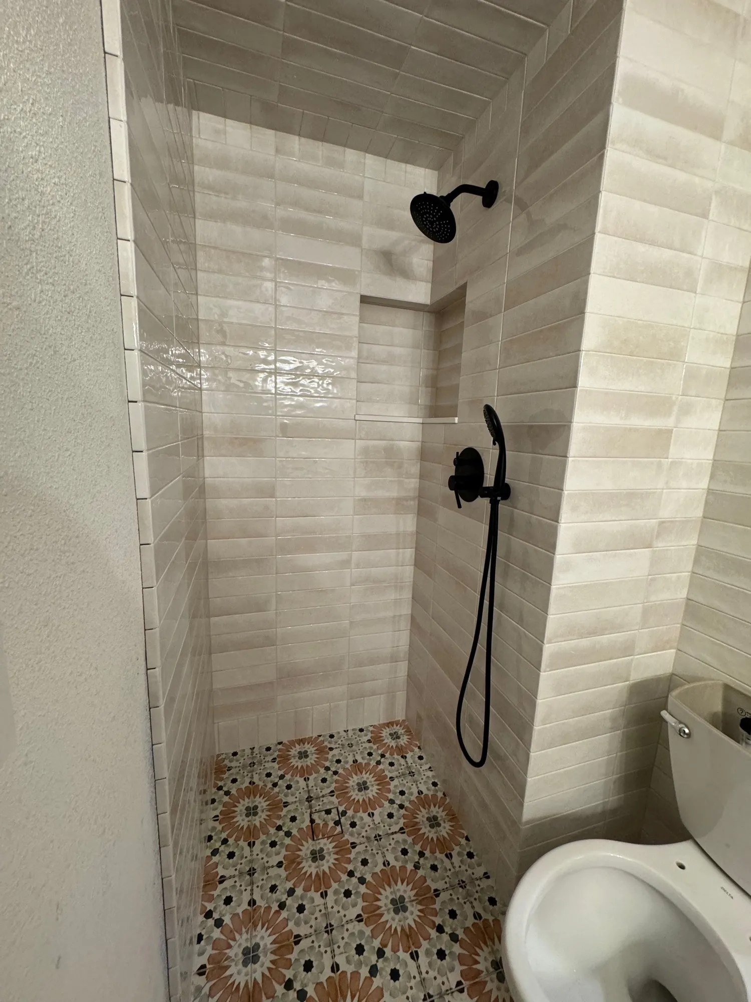 Walk-in shower with cream vertical tile walls and a floral encaustic tile floor